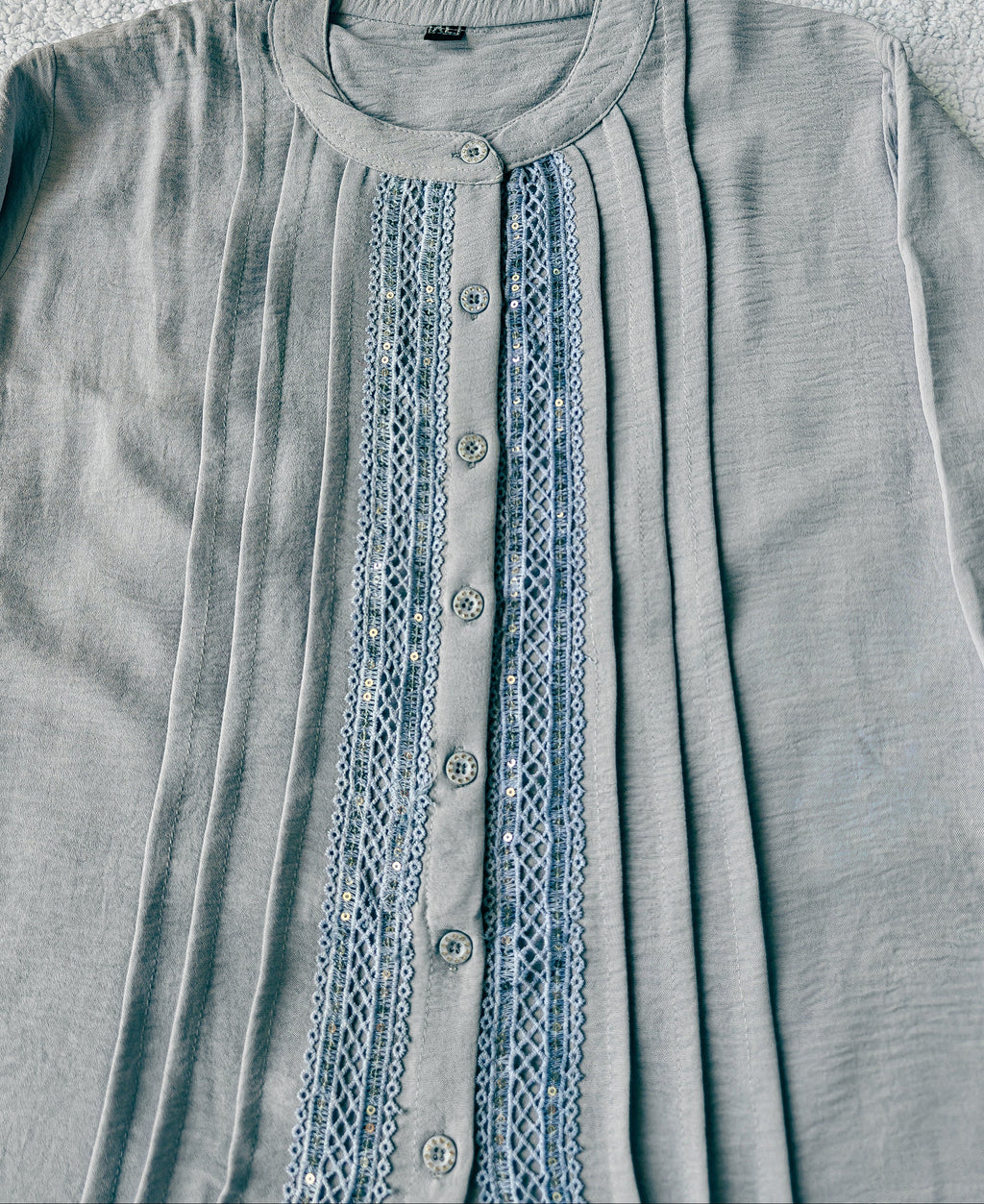 Light blue shirt with lace detailing on a textured surface