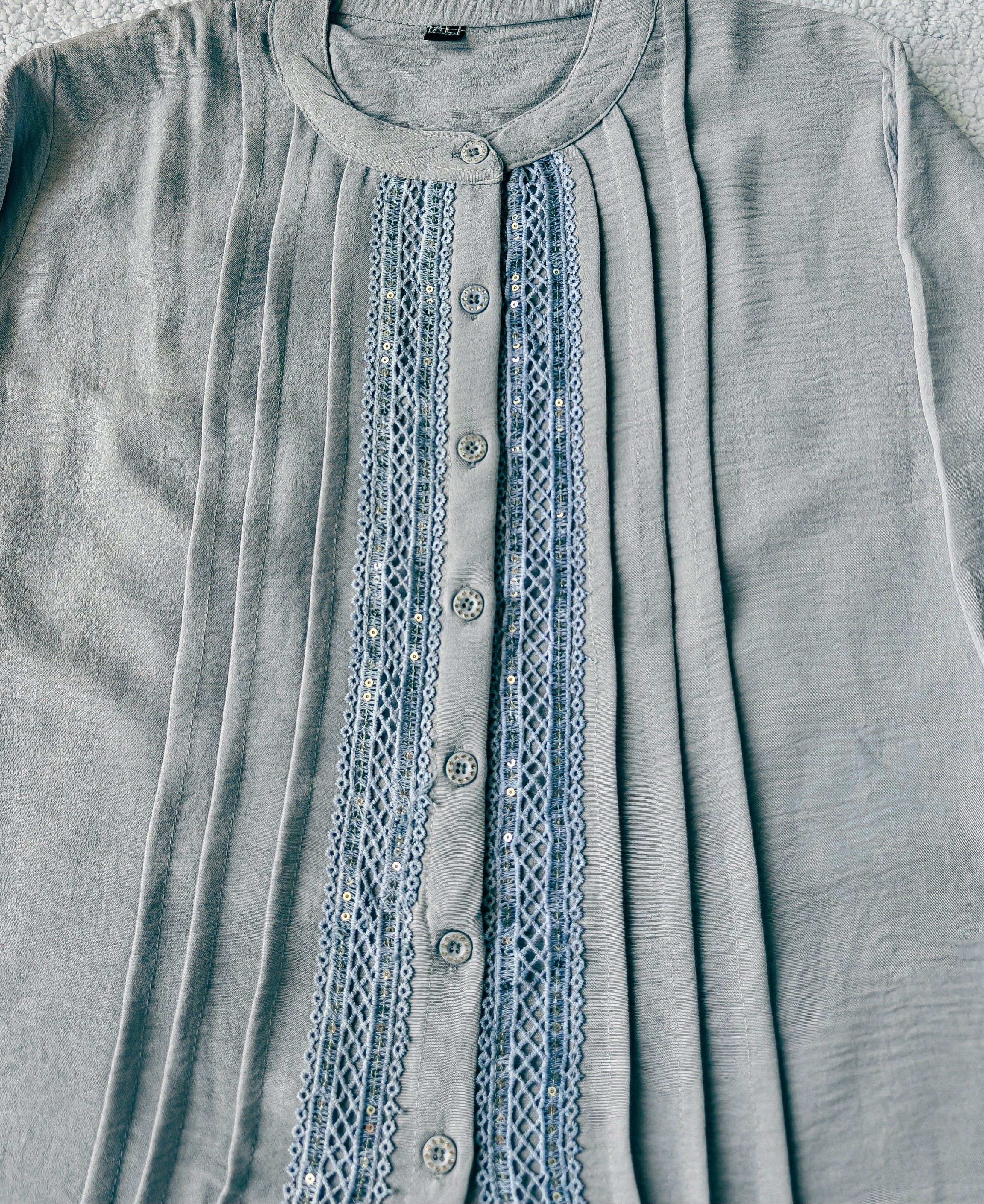 Light blue shirt with lace detailing on a textured surface