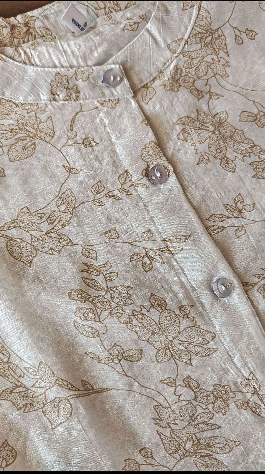 Close-up of a beige floral-patterned shirt with buttons.