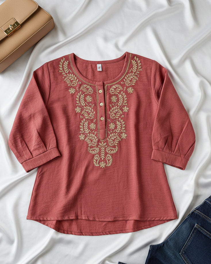 Coral Pink blouse with gold embroidery on a white fabric background