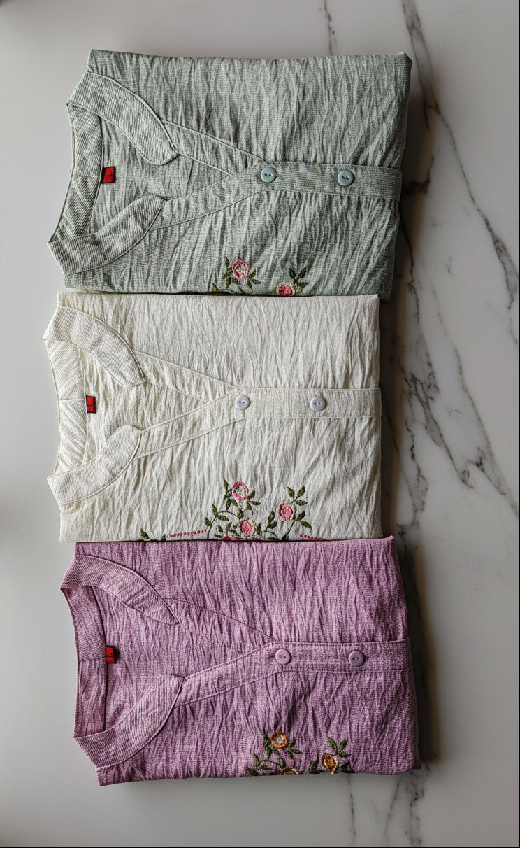 Three folded shirts in green, white, and purple with floral embroidery 