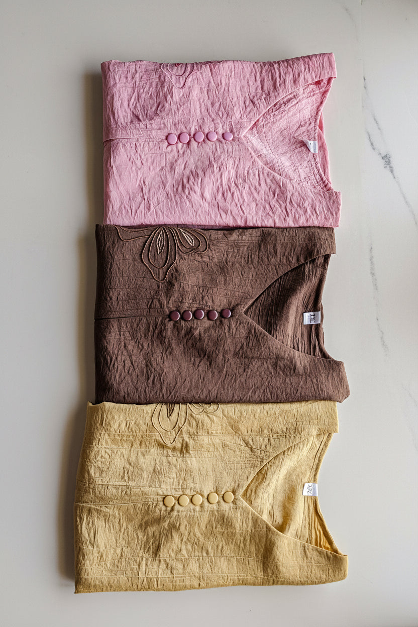 Three folded women's shirts in pink, brown, and gold 